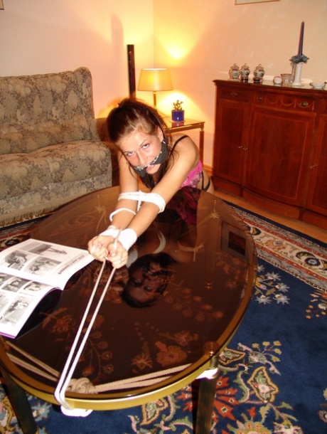 Caucasian girl sports a cleave gag while tied with rope over a coffee table 98586148